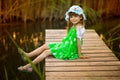 Little girl sitting on wooden bridge across river in sunny day Royalty Free Stock Photo