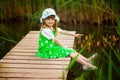 Little girl sitting on wooden bridge across river in sunny summer Royalty Free Stock Photo