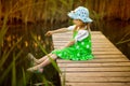 Little girl sitting on wooden bridge across river in sunny day Royalty Free Stock Photo