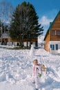 Little girl with a sled on a rope goes down the hill past a snowman