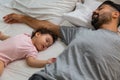 Little girl sleeping on bed near her father in bedtime. Single father get tired and sleeping together with his beloved infant Royalty Free Stock Photo