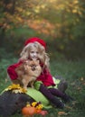 A little girl with a small red dog in the autumn forest sitting on a log next to pumpkins. Autumn photography.