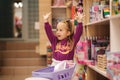 Little girl with small shopping cart in kids mall. Happy girl choosing what to buy in toy store