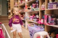 Little girl with small shopping cart in kids mall. Happy girl choosing what to buy in toy store