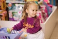 Little girl with small shopping cart in kids mall. Happy girl choosing what to buy in toy store