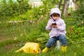 A little girl with a smartphone in her hand in the garden near a picturesque flower bed with hostas. Royalty Free Stock Photo