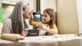 Little girl smearing laughing grandmother with flour at home