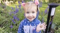 A white little pretty girl smiles joyfully and holds a small frog in a cute palm against the background of a lawn with flowers Royalty Free Stock Photo