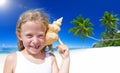 Little Girl Smiling at Camera by the Beach with Seashell Against her Ears