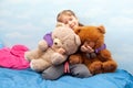 Little girl, smiling child sitting on the bed hugging two big teddy bears, cheerful kid holding her two toys close, clouds Royalty Free Stock Photo