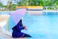 Little girl smiling near in swimming pool and holding colourful umbrella in hands. children playing in swimming pool on summer Royalty Free Stock Photo