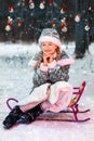 Little girl smiling in the new year forest on a sled. Snow Maiden in a festive costume. winter, snow is falling. toys on the tree