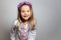 Little girl smiling  in white dress and purple wreath on gray isolated background. Happiness emotion concept Royalty Free Stock Photo