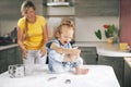 A little girl, soiled in flour, sits on the table and laughs. A girl plays with flour. Blurred background, space for
