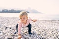 Little girl squatted down and reached for a pebble on a pebble beach