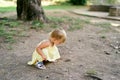 Little girl squatted near a hole in the ground near a tree