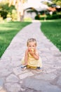 Little girl squatting on a paved path in the park and nibbling an apple Royalty Free Stock Photo