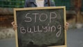 Little girl standing demonstrating alone holding and raising schoolboard with text stop bullying on the street near