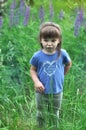 Little girl standing upset in sunny blooming forest. Toddler child picking lupine flowers. Kids play outdoors. Summer fun for fami Royalty Free Stock Photo