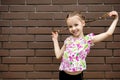 A little girl stands against a brick wall and playfully holds her pigtails Royalty Free Stock Photo