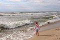 A little girl stands against the waves.