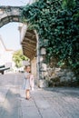 Little girl stands at an arched passage in a stone wall entwined with green ivy, hugging a pink toy rabbit Royalty Free Stock Photo