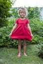 little girl stands in the backyard in a red dress and spreads th Royalty Free Stock Photo