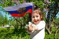 Little girl stands with flag of Russia in front of lilac Bush on sunny day Royalty Free Stock Photo
