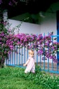 Little girl stands on green grass near a metal fence of a house next to a purple bougainvillea bush Royalty Free Stock Photo