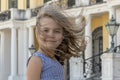 A little girl stands with her hair fluttering in the wind against the backdrop of a historic building. Royalty Free Stock Photo