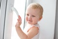 Baby is trying to open the window in the apartment. No lock on the window. Dangerous home for a baby. Fall safety for children. Royalty Free Stock Photo