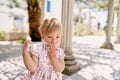 Little girl stands near a column and gnaws a bottle of water