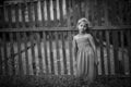 Little girl stands near a fence in the village. Black and white photo. Royalty Free Stock Photo