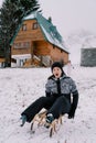 Little girl stands near the house and looks at her screaming mom going down the hill on a sled Royalty Free Stock Photo