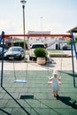 Little girl stands near the swing on the playground and holds on to the chains