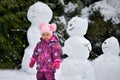 A little girl stands near three snowmen in the winter