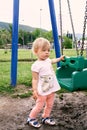 Little girl stands on the playground and holds the swing with her hand Royalty Free Stock Photo