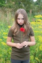 A little girl stands with a red flower behind her ear outside