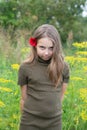 A little girl stands with a red flower behind her ear outside