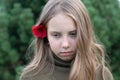 A little girl stands with a red flower behind her ear outside