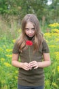 A little girl stands with a red flower behind her ear outside