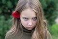 A little girl stands with a red flower behind her ear outside