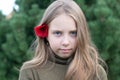 A little girl stands with a red flower behind her ear outside