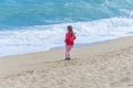 A little girl stands on a sandy beach and looks at the waves of the sea. Royalty Free Stock Photo