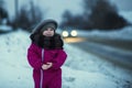 .A little girl stands in the snow by the road in the evening