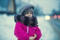 .A little girl stands in the snow by the road in the evening