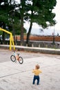 Little girl stands on a tiled playground in front of a bicycle in a park Royalty Free Stock Photo