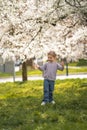 Little girl stands under a blooming apple tree. The wind blows and flower petals fly like snow in Prague park, Europe Royalty Free Stock Photo