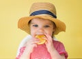 Little girl in a straw hat eats a lemon on a yellow background Royalty Free Stock Photo