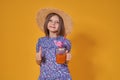 Little girl in a straw hat and sunglasses is smiling on a yellow background. child girl in a blue dress is holding a Royalty Free Stock Photo